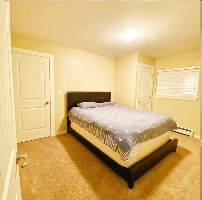 A bed with a blue and white comforter is in a room with carpeted flooring and white walls.