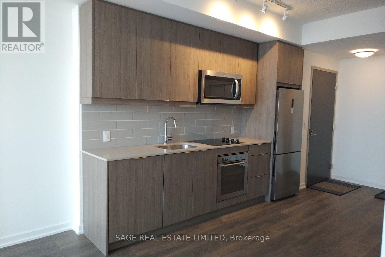 A kitchen with a refrigerator, microwave, oven and sink.