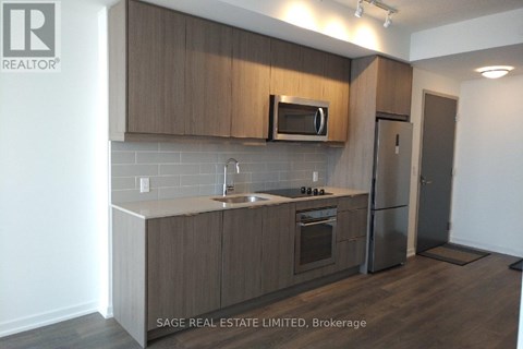 A kitchen with a refrigerator, microwave, oven and sink.
