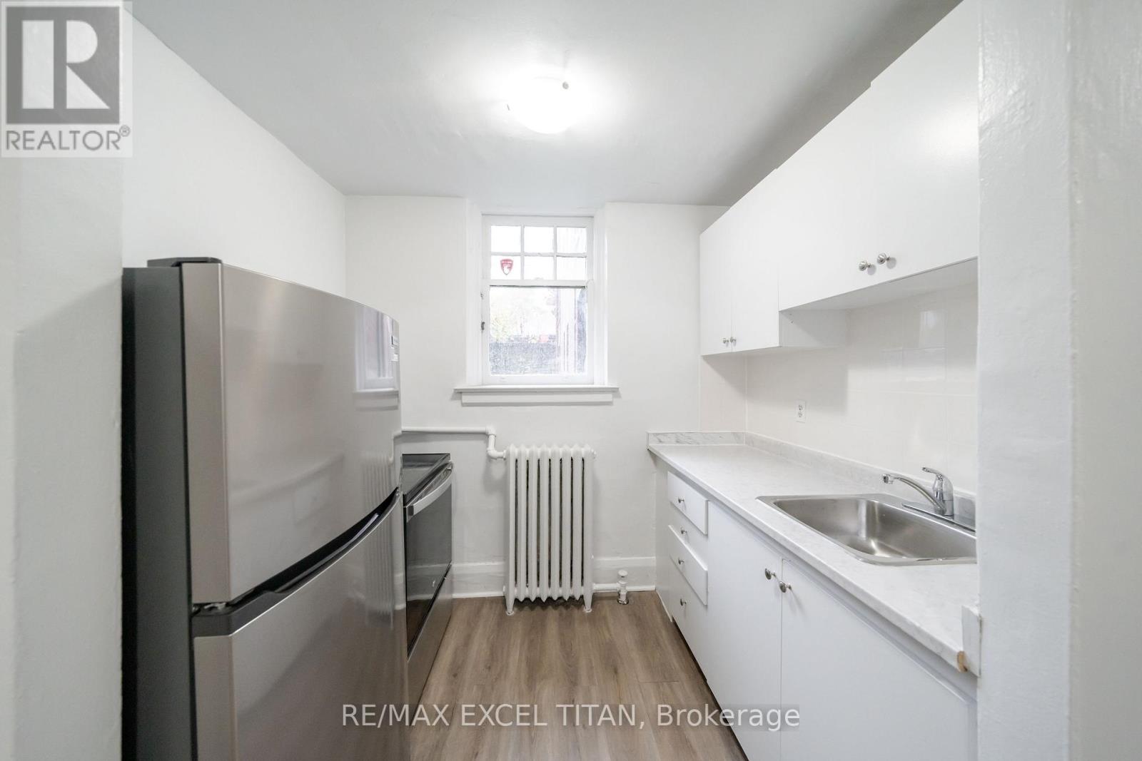 A white kitchen with a refrigerator, sink, and cabinets.