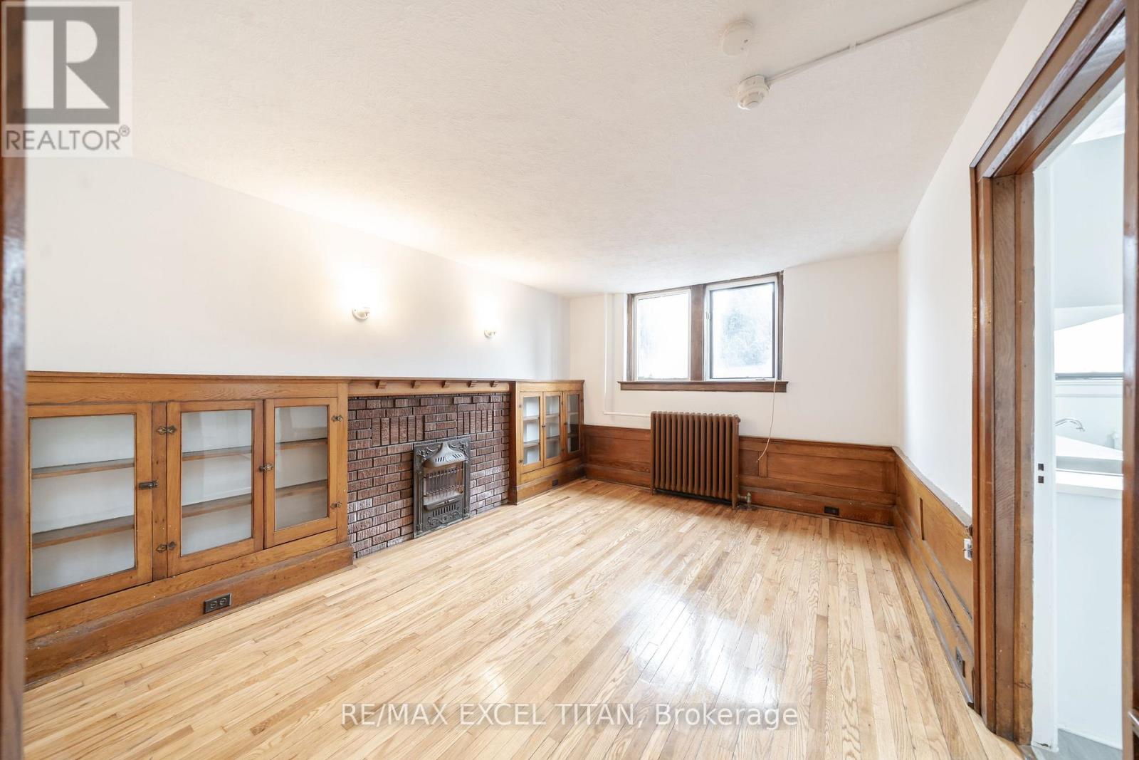A large, empty room with wood flooring and a fireplace.