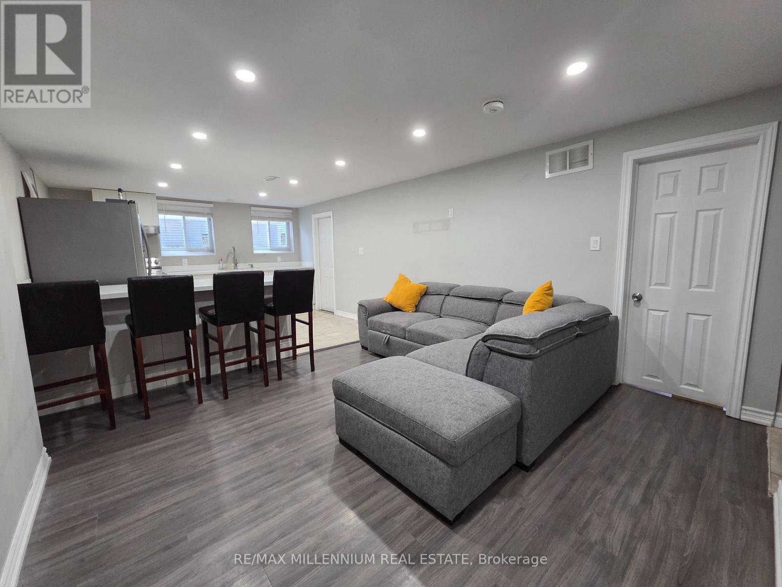 A well-lit living room with a grey sofa and a dining table with chairs.