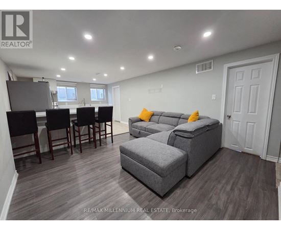 A well-lit living room with a grey sofa and a dining table with chairs.