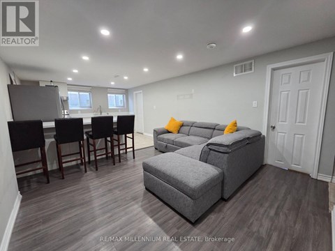 A well-lit living room with a grey sofa and a dining table with chairs.