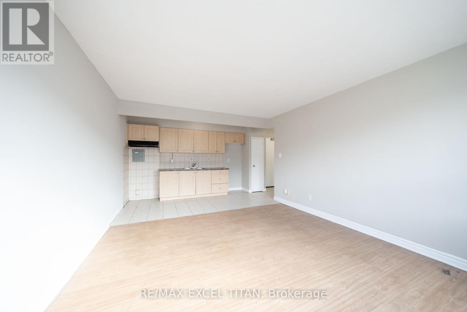A white room with a small kitchenette and wooden floors.