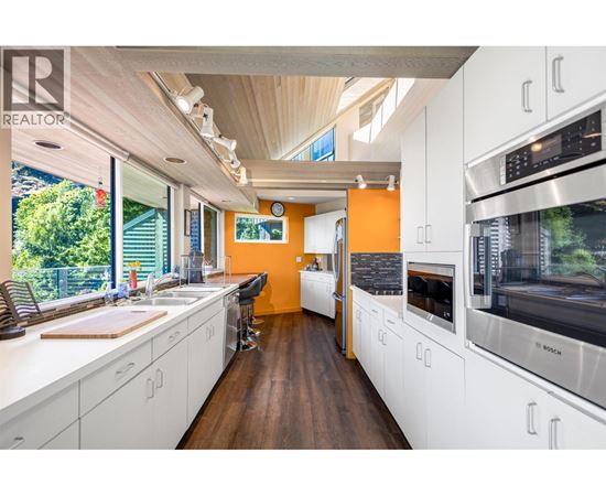 A modern kitchen with white cabinets and a wooden floor.