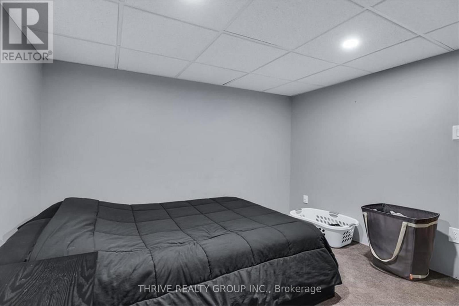 A bedroom with a bed covered in a black quilted comforter and a laundry basket on the floor.
