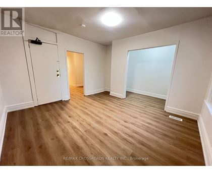 A room with wooden flooring and white walls, with a door on the left and a large window on the right.