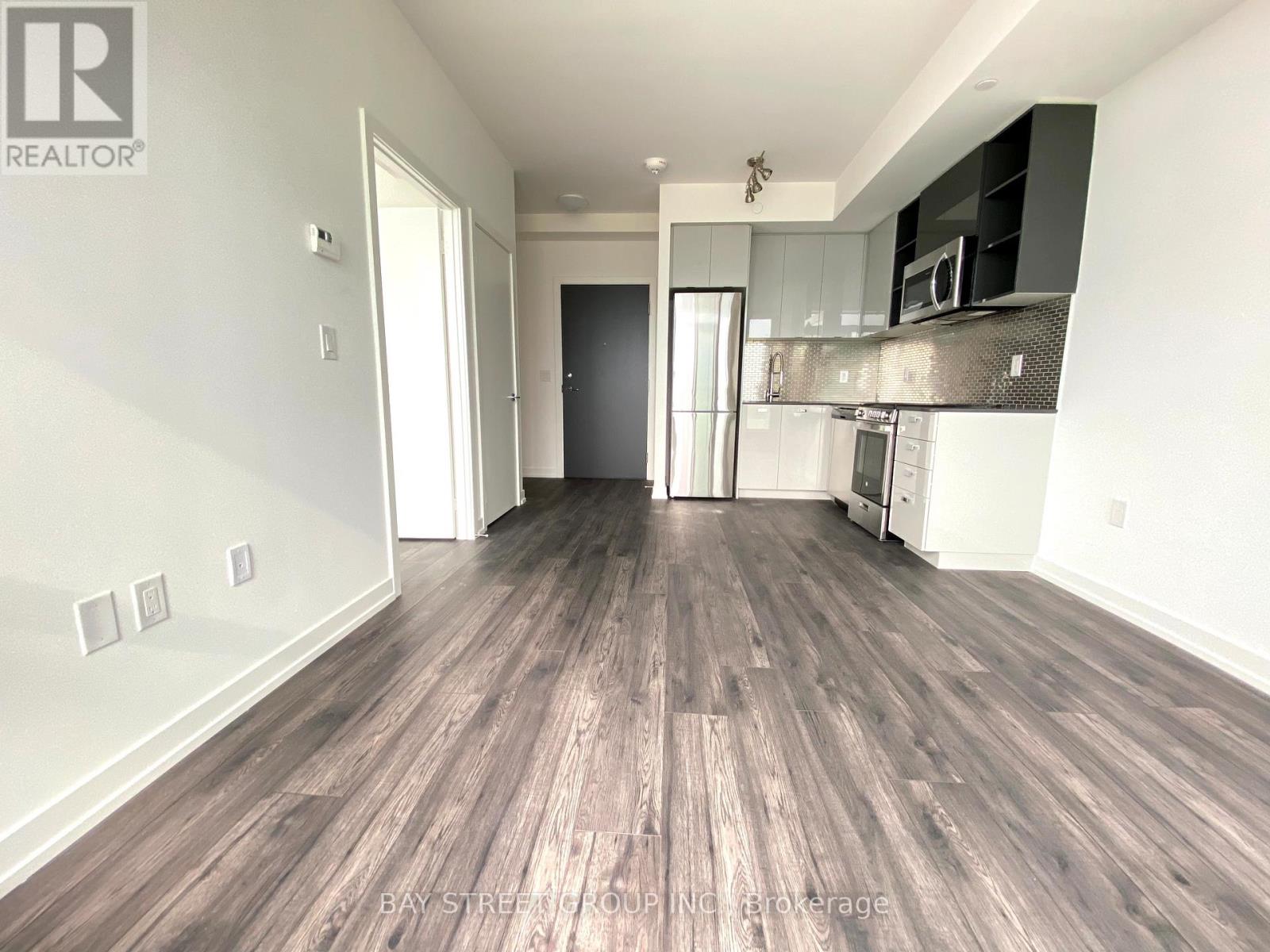 A spacious room with wooden flooring and a kitchen area in the background.