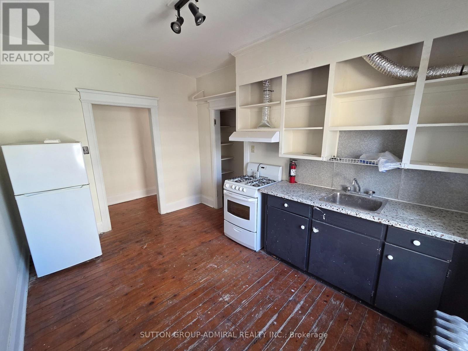 A kitchen with a white fridge, black cabinets, and a wooden floor.