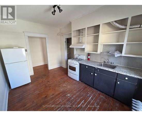 A kitchen with a white fridge, black cabinets, and a wooden floor.
