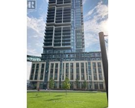 A tall building with a glass facade stands in front of a smaller building with a metal framework.