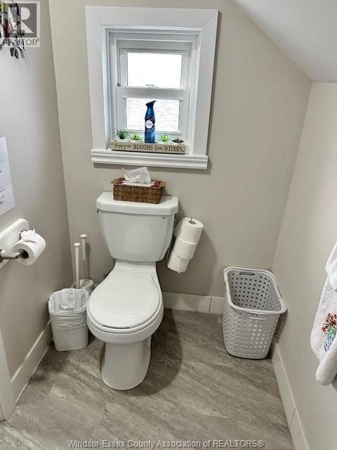 A white toilet in a small bathroom with a window above it.