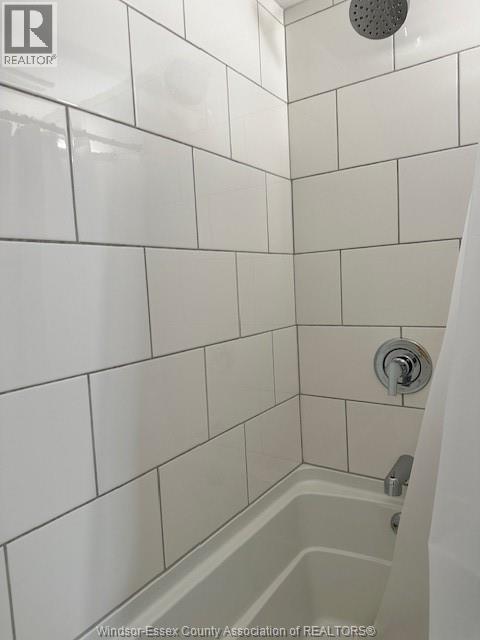 A white tiled shower with a shower head and a faucet.