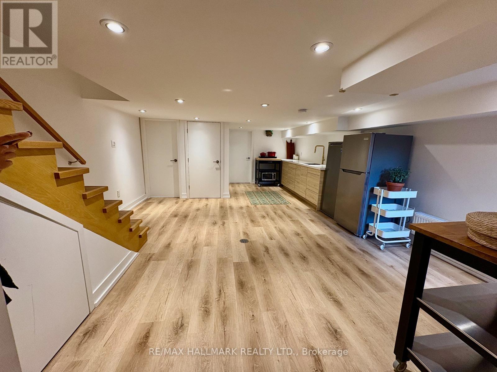 A spacious room with wooden flooring and a staircase on the left side.