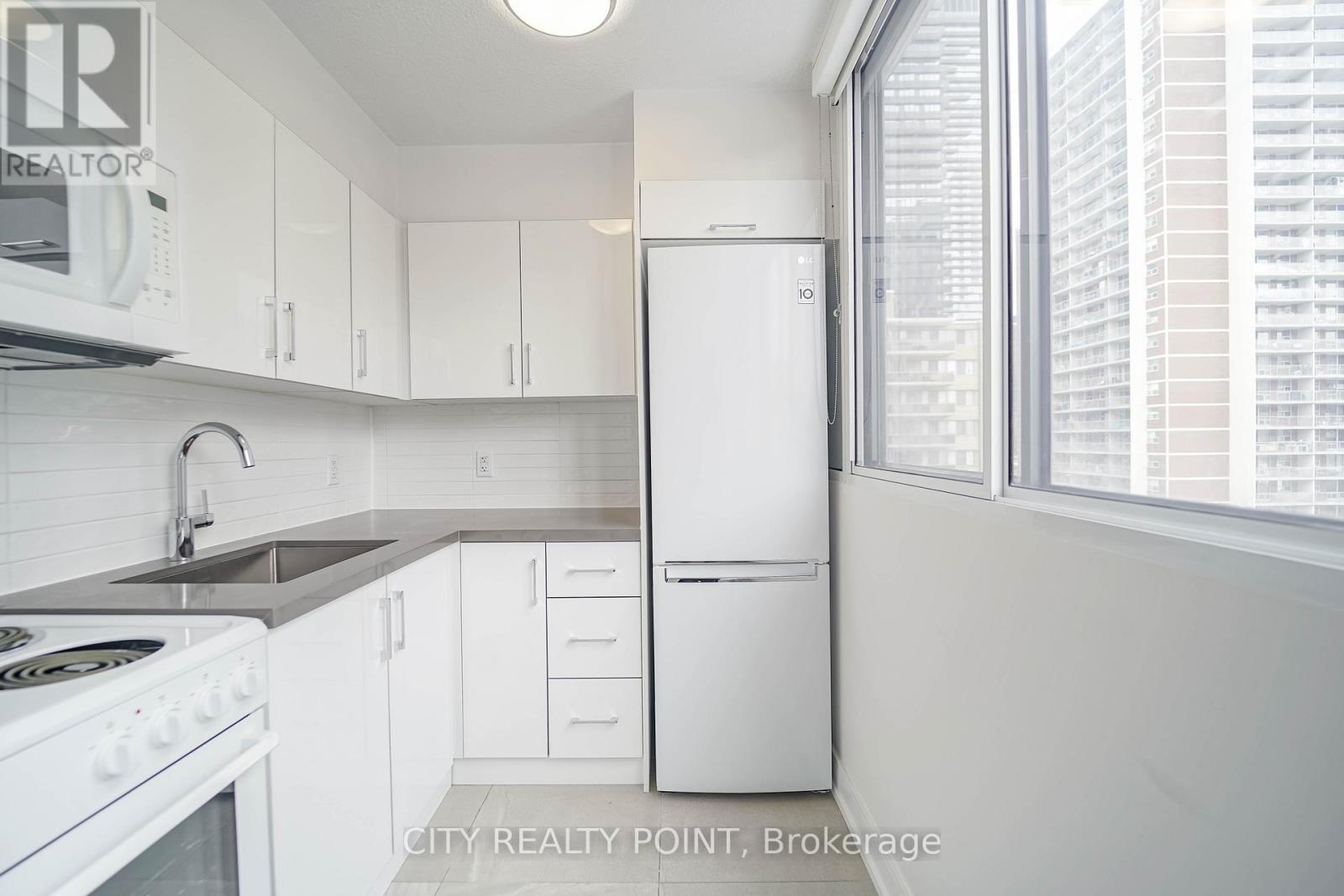 A white kitchen with a refrigerator, stove, and sink.