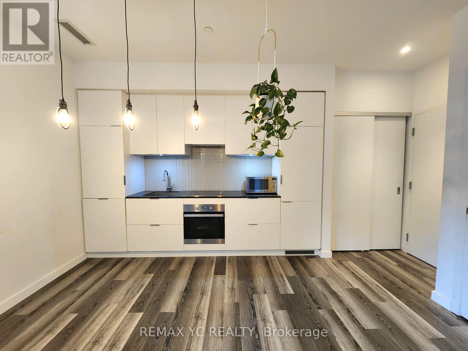 A modern kitchen with white cabinets and a wooden floor.