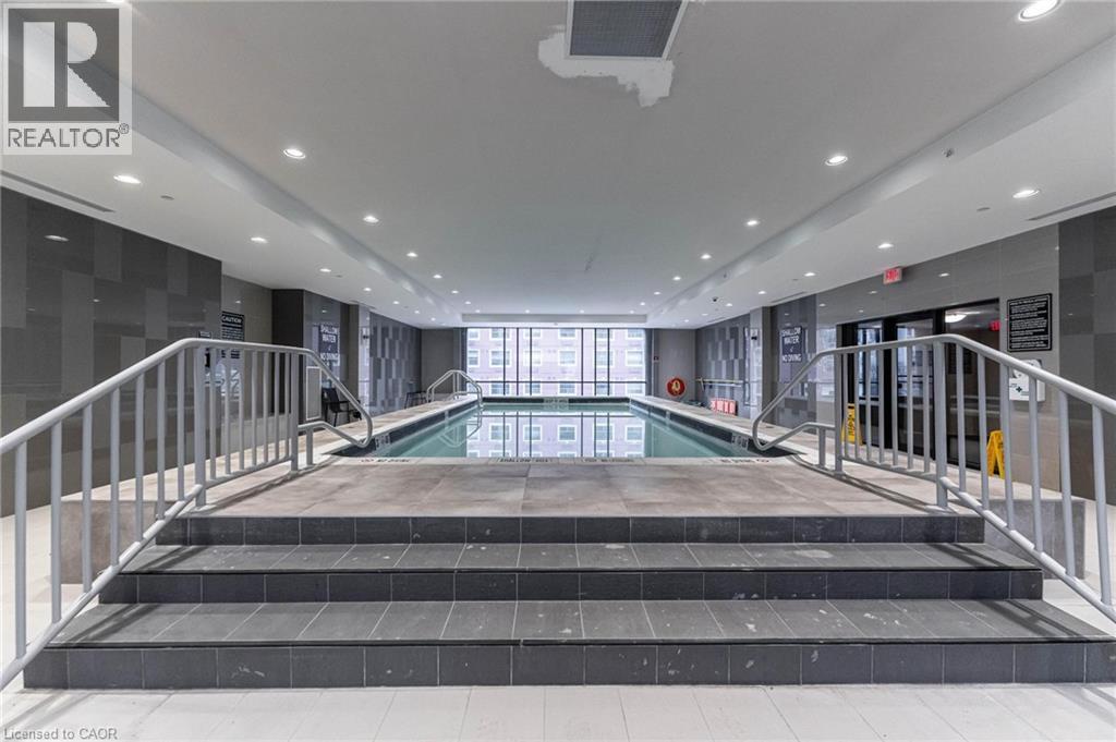 A large indoor swimming pool with a glass enclosure and a metal railing.