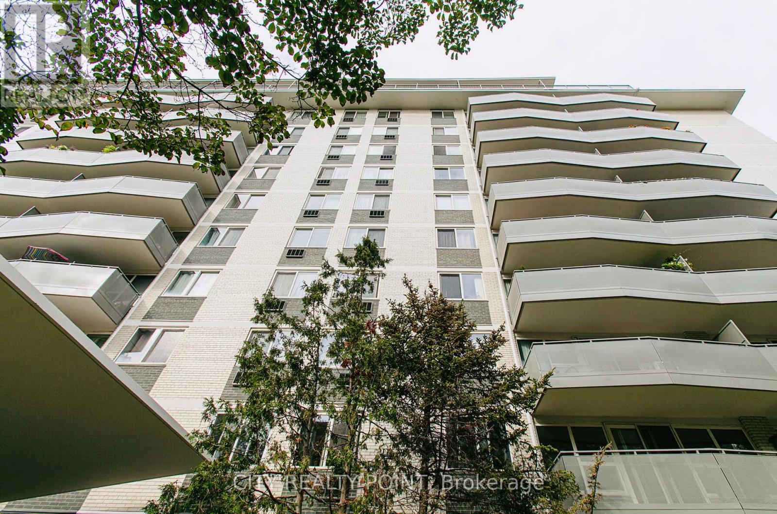 A tall building with balconies and trees in front.