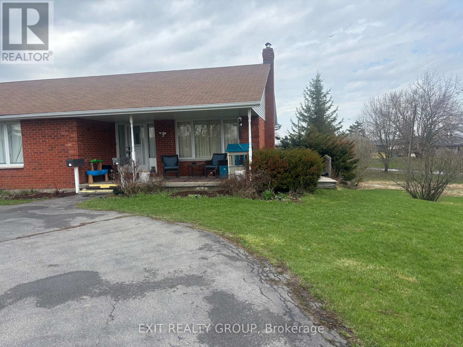 A house with a red brick exterior and a white roof is shown with a sign that reads "EXIT REALTY GROUP, Brokerage".