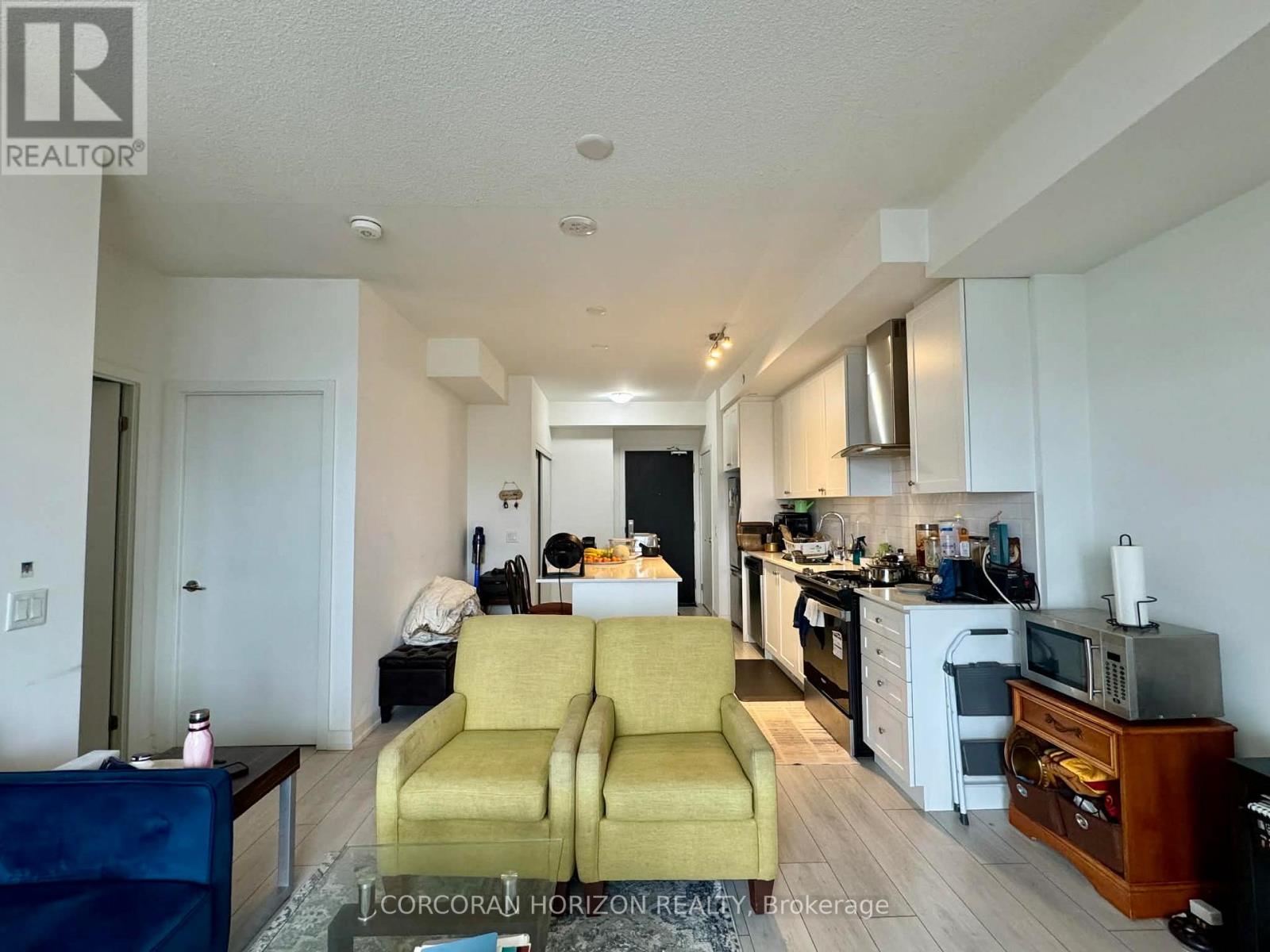 A living room with a yellow couch and a kitchen area in the background.