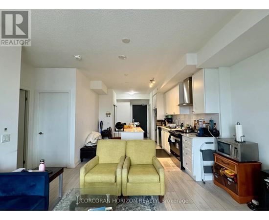 A living room with a yellow couch and a kitchen area in the background.