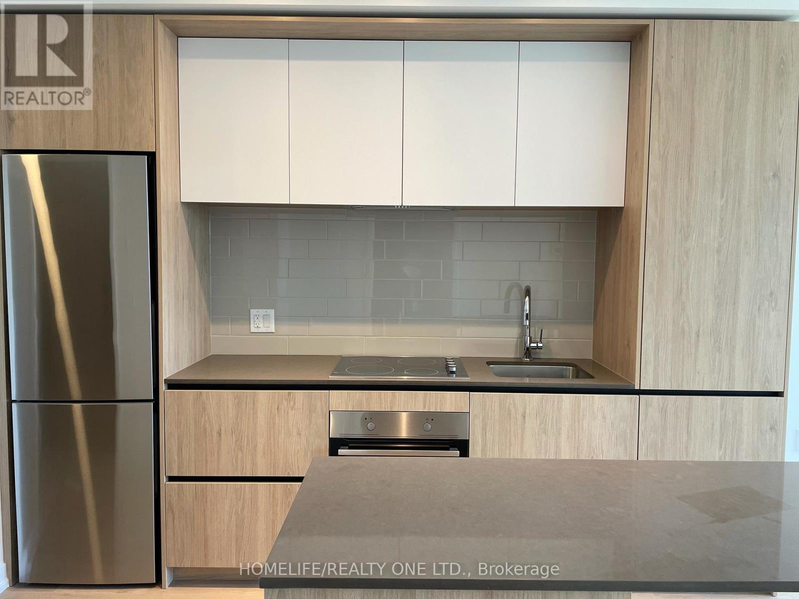 A modern kitchen with wooden cabinets and a stainless steel refrigerator.