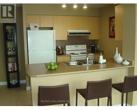 A kitchen with a white fridge, brown chairs and a sink.