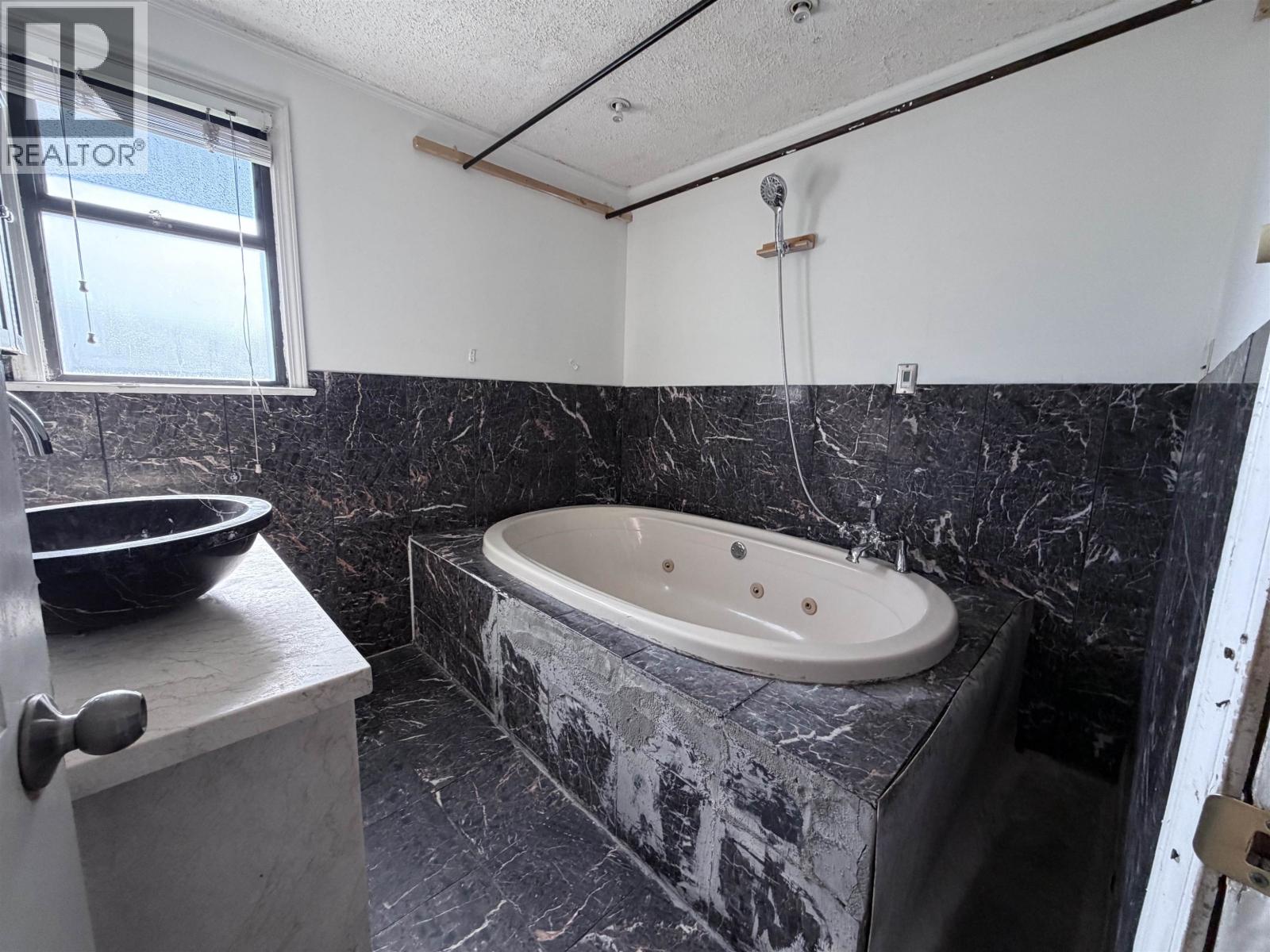 A bathroom with a marble tub surround and a bowl on the counter.