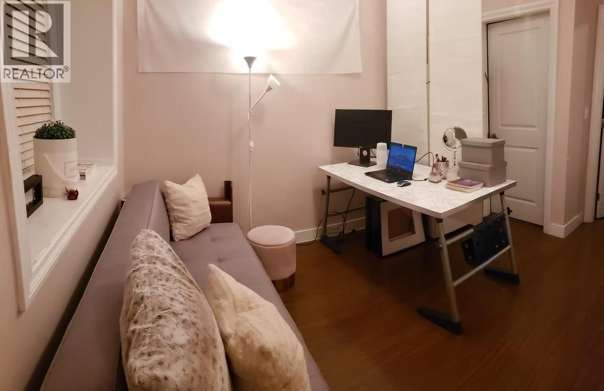 A room with a grey couch, a desk with a laptop and a lamp.