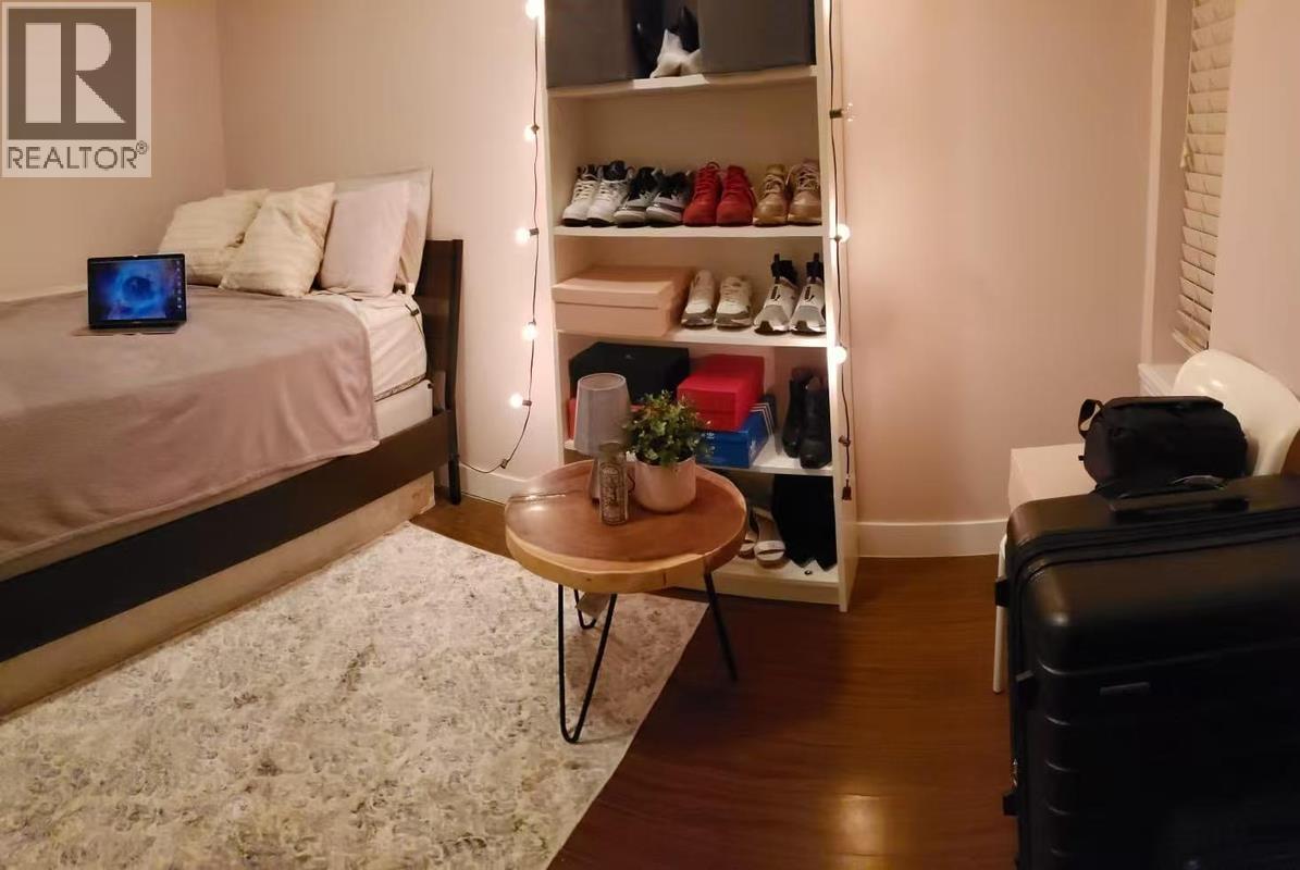 A bedroom with a bed, a shoe rack, a table, and a suitcase.