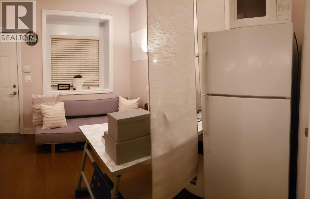 A white refrigerator stands in a kitchen with a table and a couch in the background.