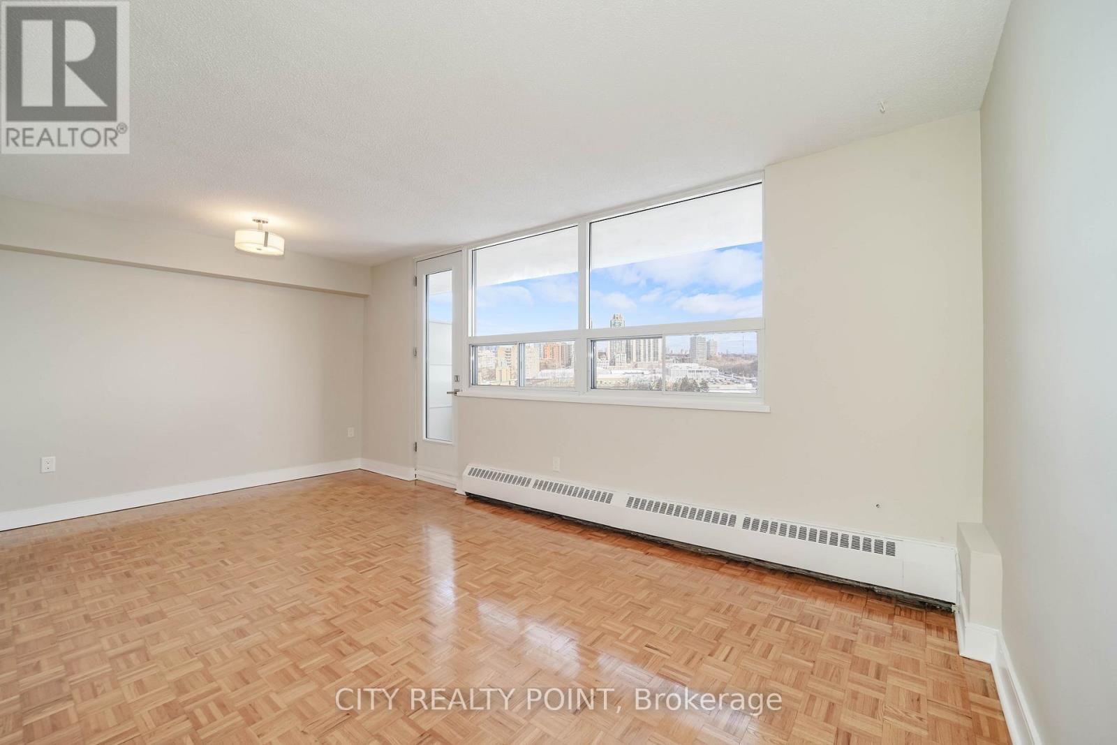 A room with a wooden floor and a window overlooking a cityscape.