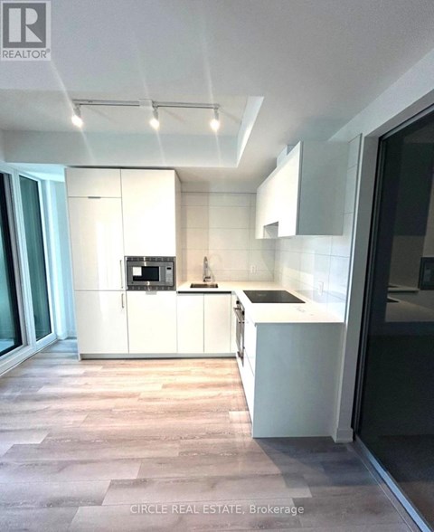 A modern kitchen with white cabinets and a wooden floor.