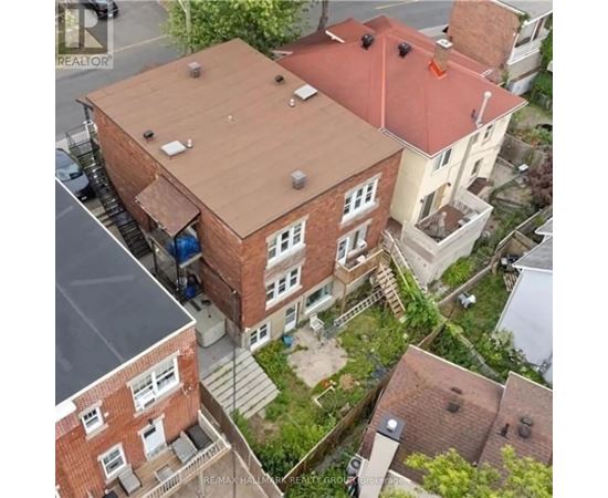 A red brick building with a brown roof is surrounded by other buildings.