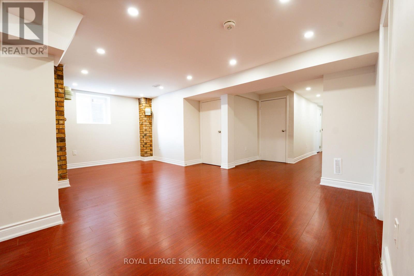 A spacious room with wooden floors and white walls, with a logo that reads "REALTOR" on the top left corner.