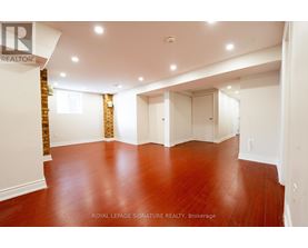 A spacious room with wooden floors and white walls, with a logo that reads "REALTOR" on the top left corner.