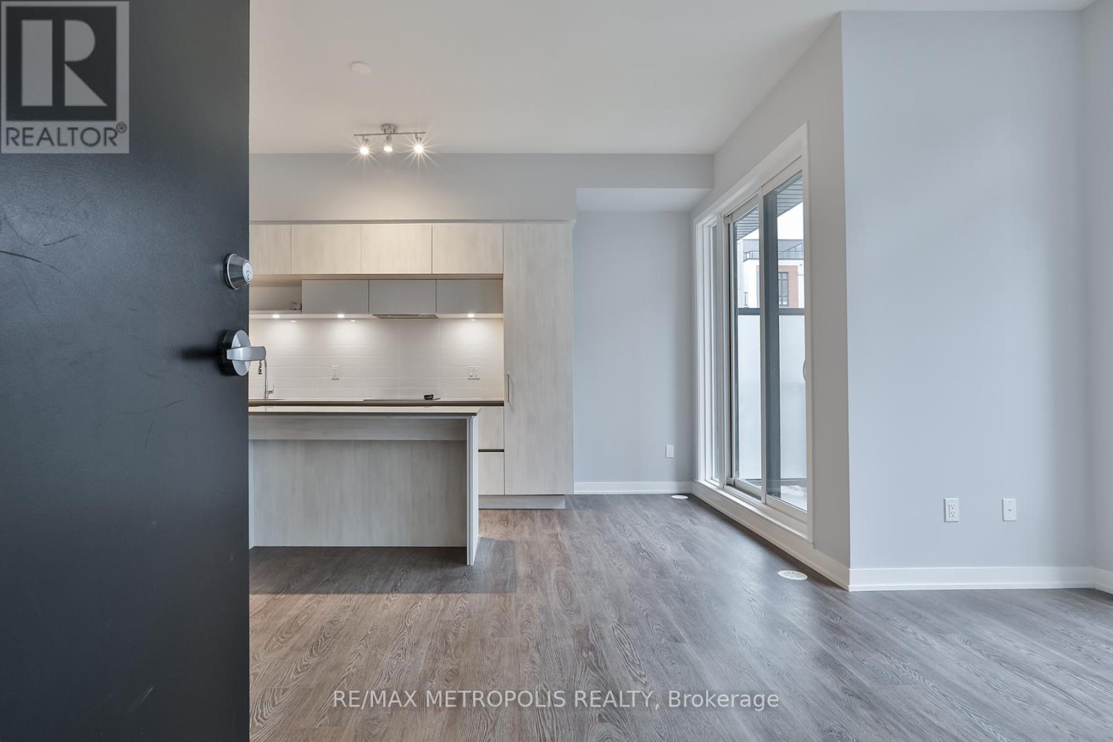 A room with a grey floor and white walls, with a black door on the left and a window on the right.