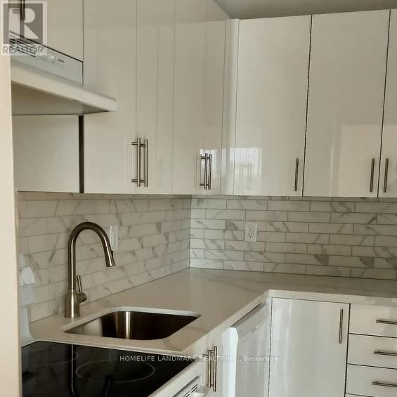 A kitchen with white cabinets and a marble backsplash.