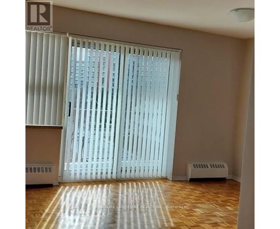 A room with a window covered by white blinds and a wooden floor.