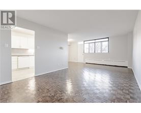 A spacious room with wooden flooring and white walls, part of a real estate listing.