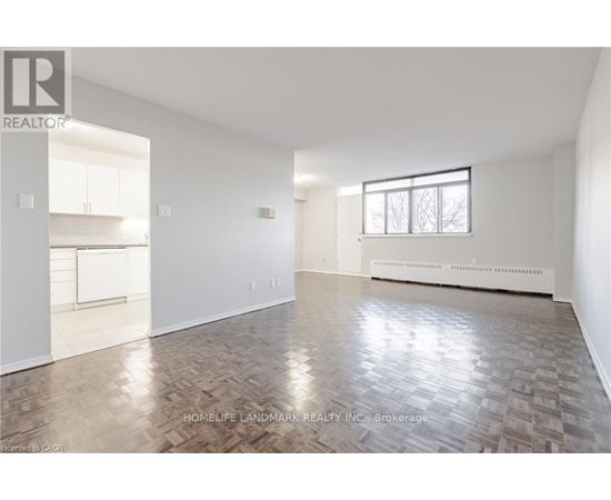 A spacious room with wooden flooring and white walls, part of a real estate listing.