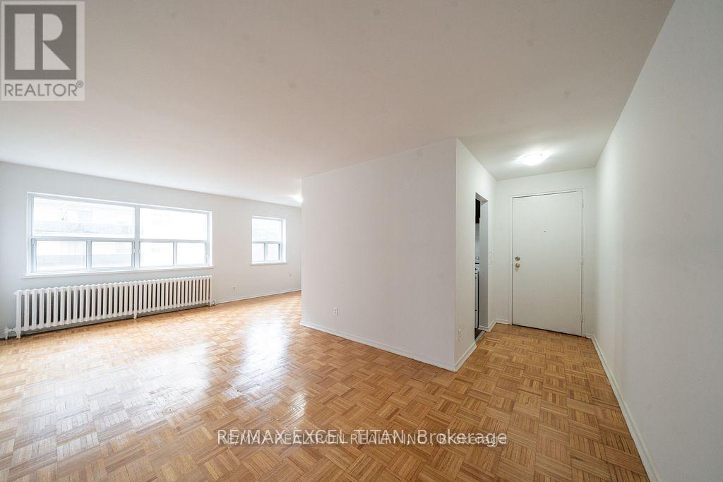 A room with wooden flooring and white walls, with a window and a door visible.