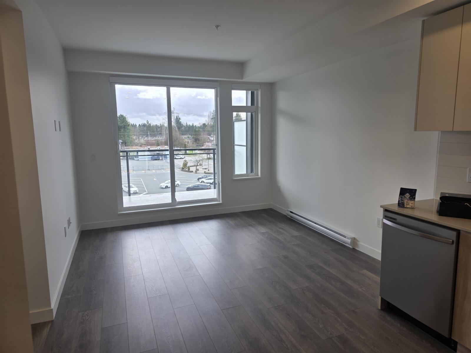 A kitchen with a refrigerator and a large window overlooking a parking lot.