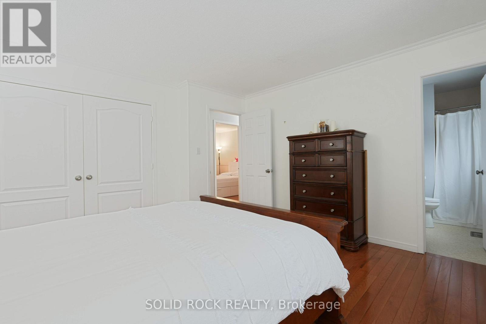 A bedroom with a white bed and wooden dresser.