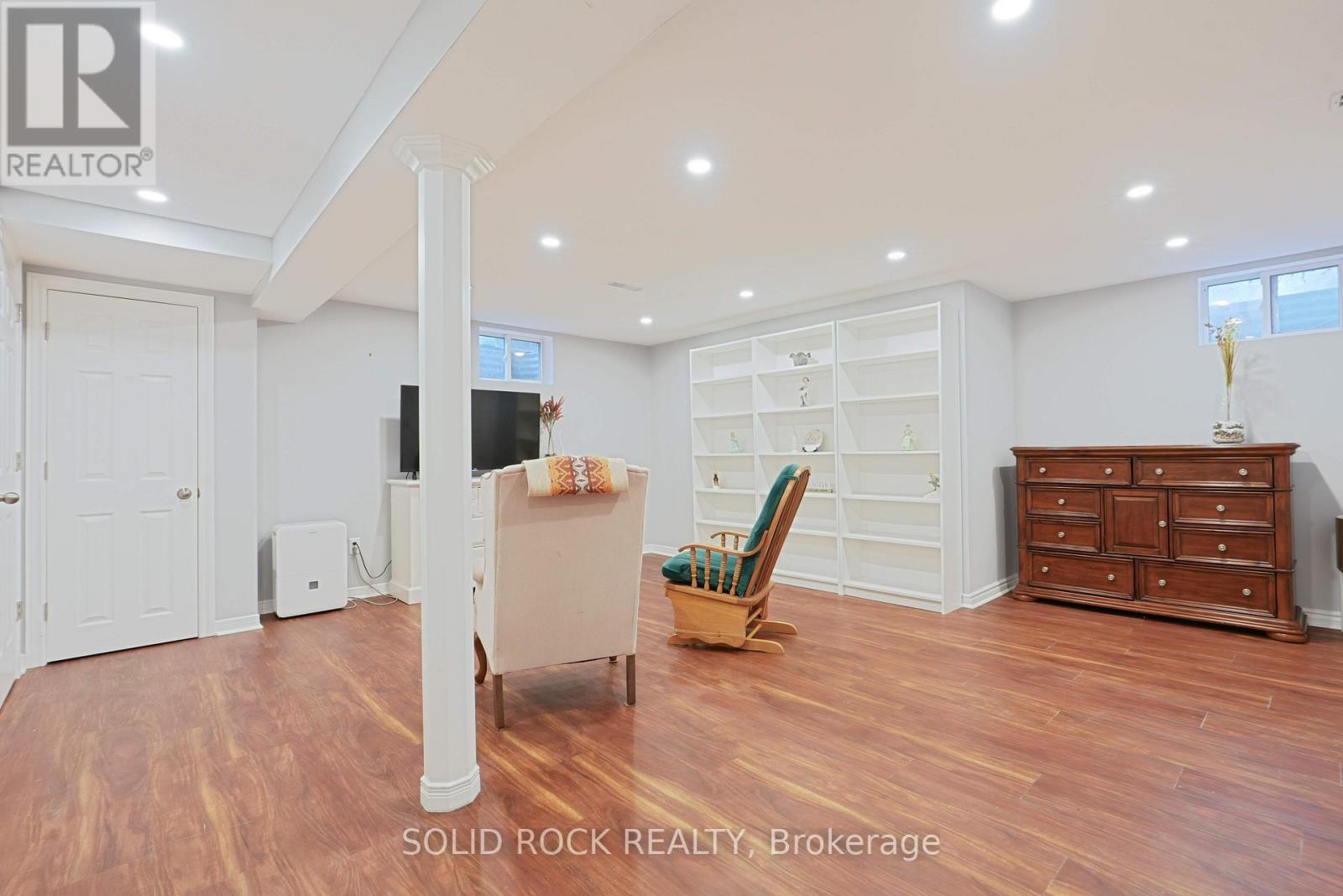 A spacious room with wooden floors and white walls, furnished with a chair, a cabinet, and a television.