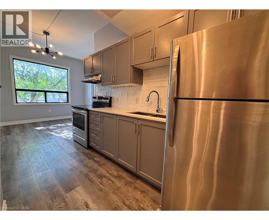 A modern kitchen with a stainless steel refrigerator and wooden flooring.