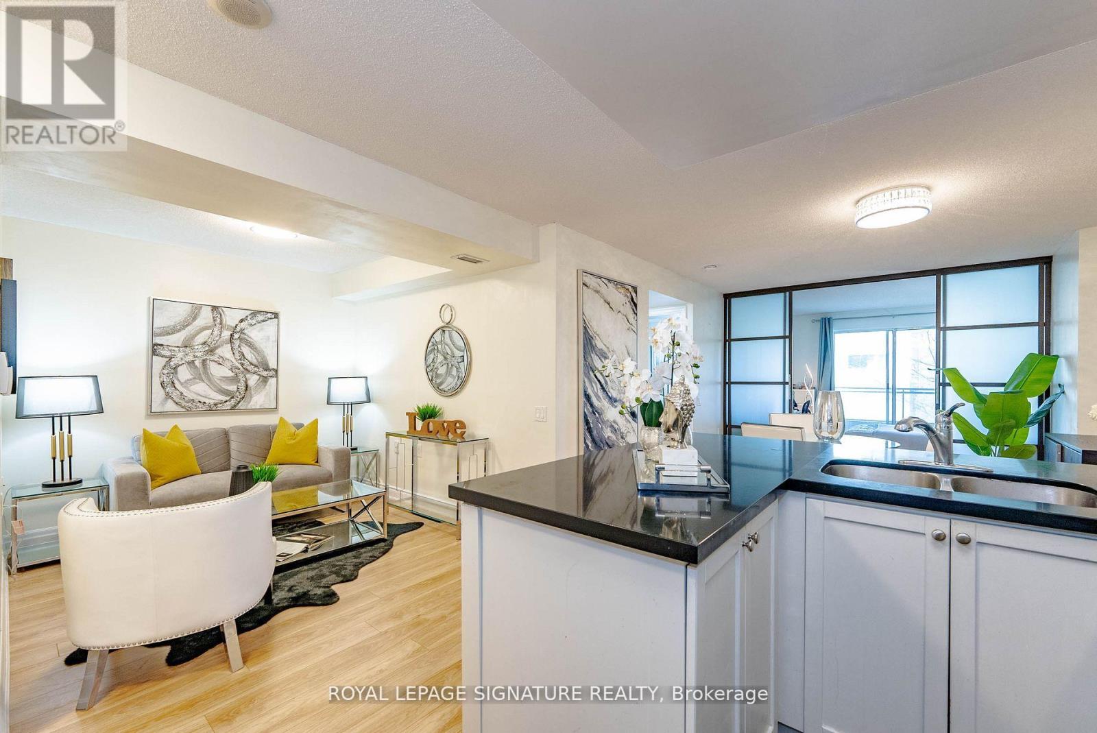 A well-lit, modern kitchen and living room with white furniture and a black countertop.