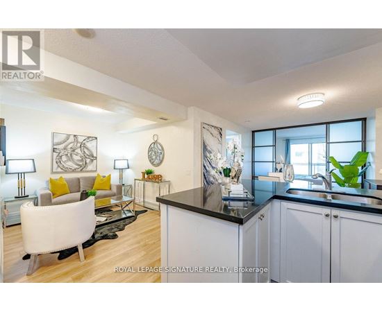 A well-lit, modern kitchen and living room with white furniture and a black countertop.