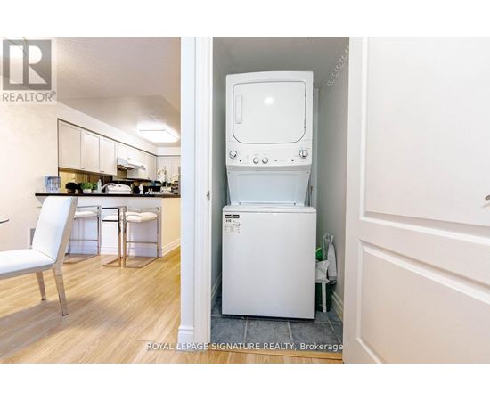 A white washing machine is in a small room with a white chair and a small kitchen.